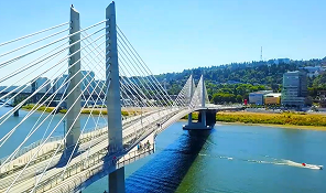 Cable-stayed bridge over a river with a boat moving on the water and green hills in the background.